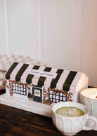 A Le Petit Café Mimi – Two Little Cups Candle Set designed to look like a cafe sits next to two lit soy candles in scalloped cups on a wooden surface.