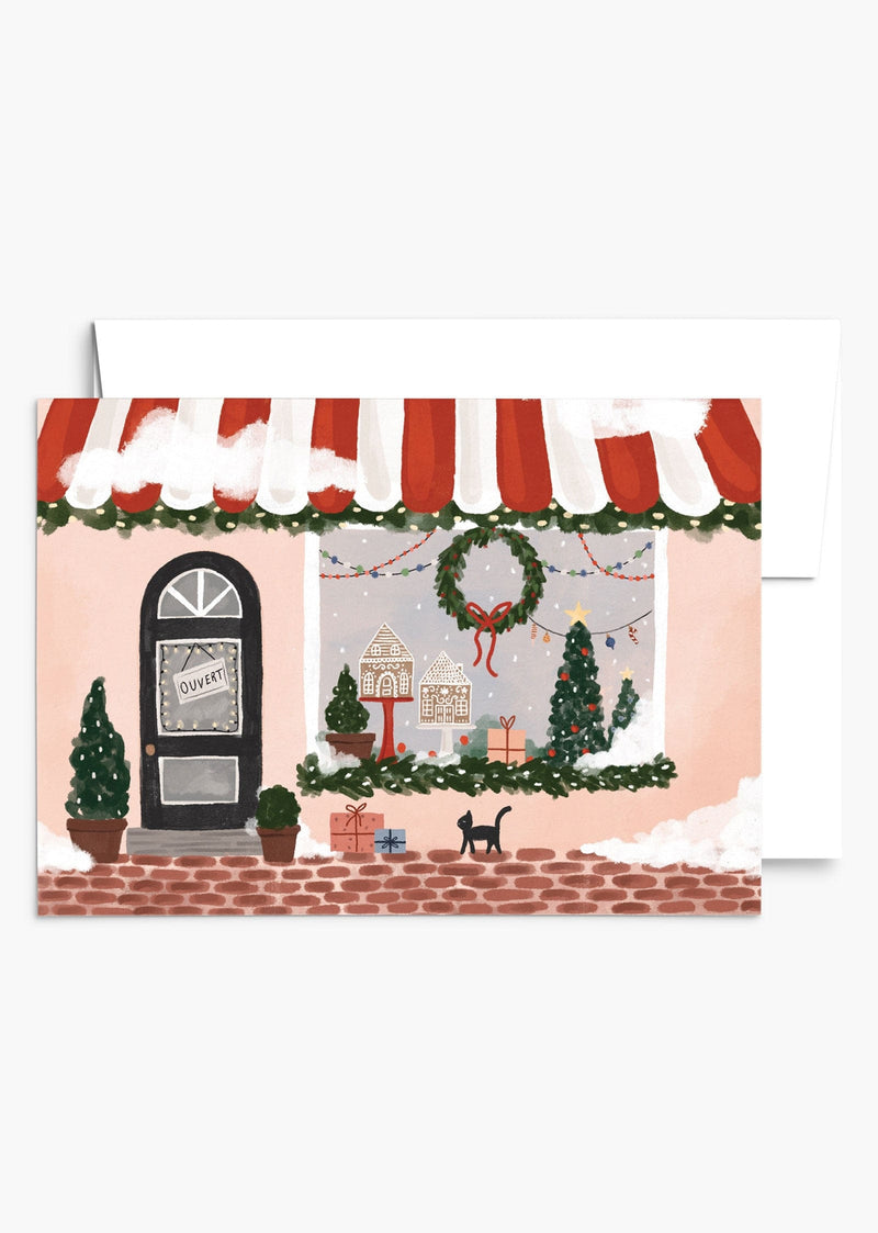 cute Christmas boutique storefront greeting card, featuring snowflakes, window with tree, gingerbread houses and a wreath. By mimi & august
