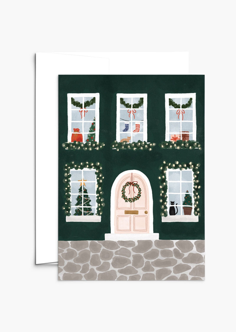 Greeting card with green holiday home with windows showing kitties, Christmas's socks and tree. By Mimi & August