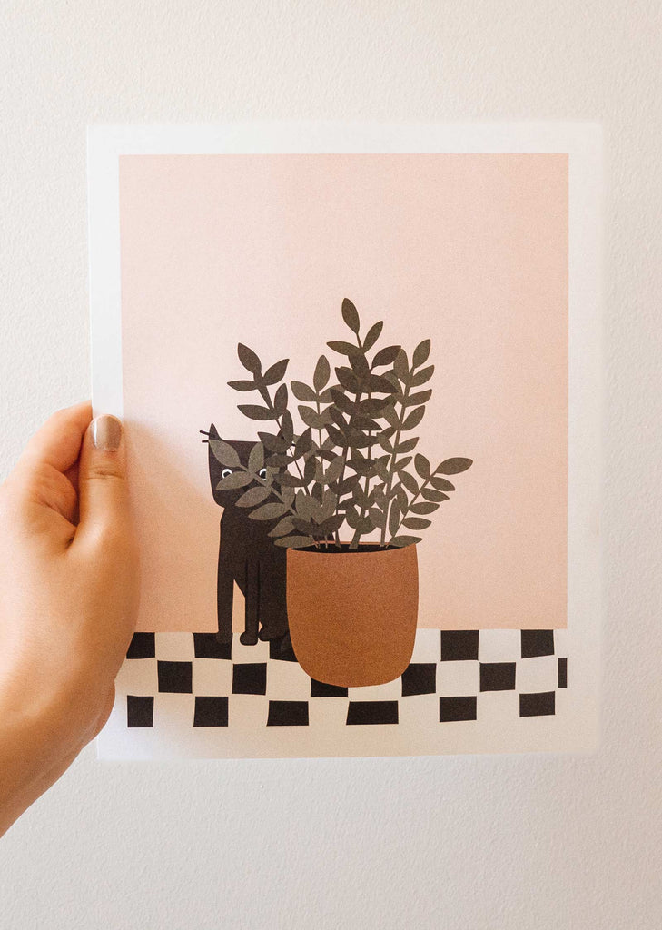 A hand holding a art print of a cat with a potted plant by mimi and august