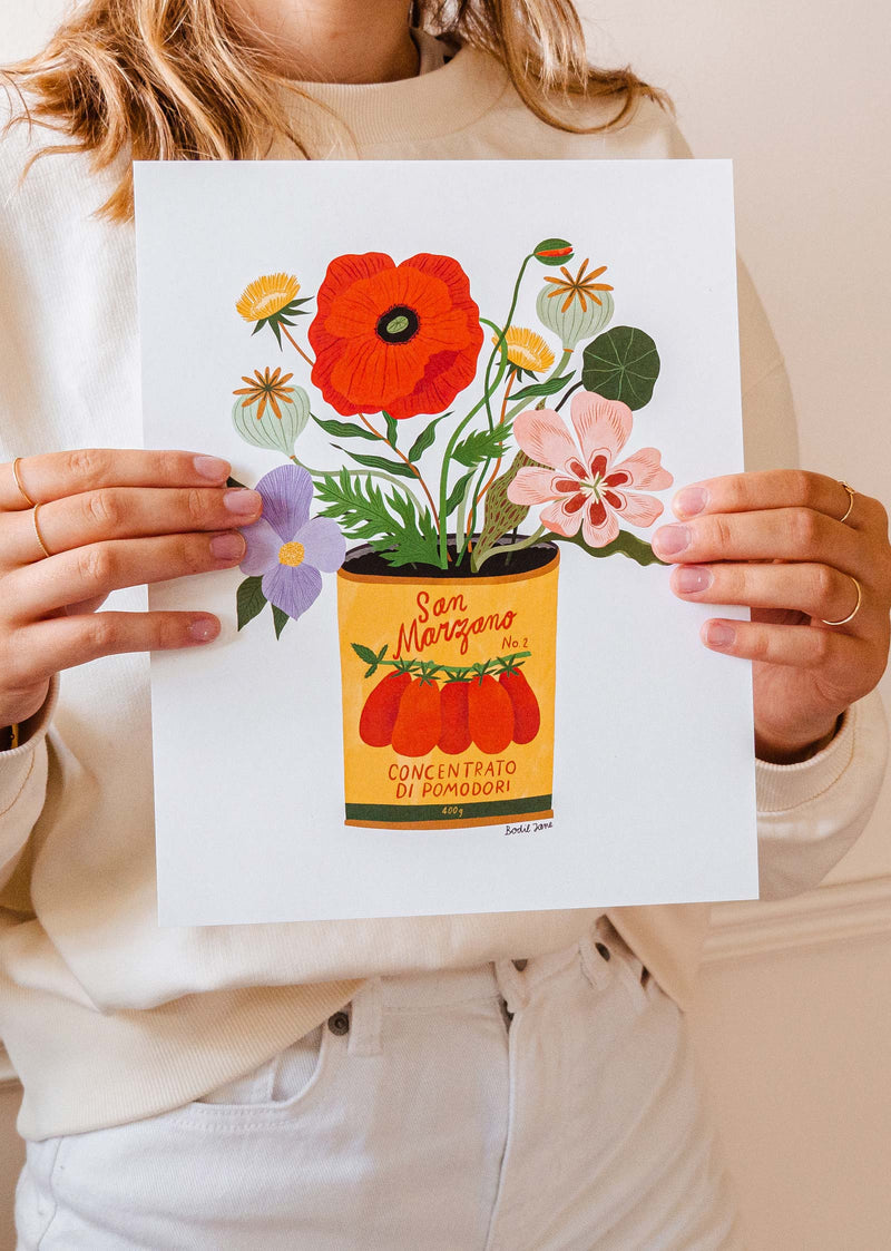 A woman holding up a Bodil Jane art print 8x10 of flowers in a tin can.