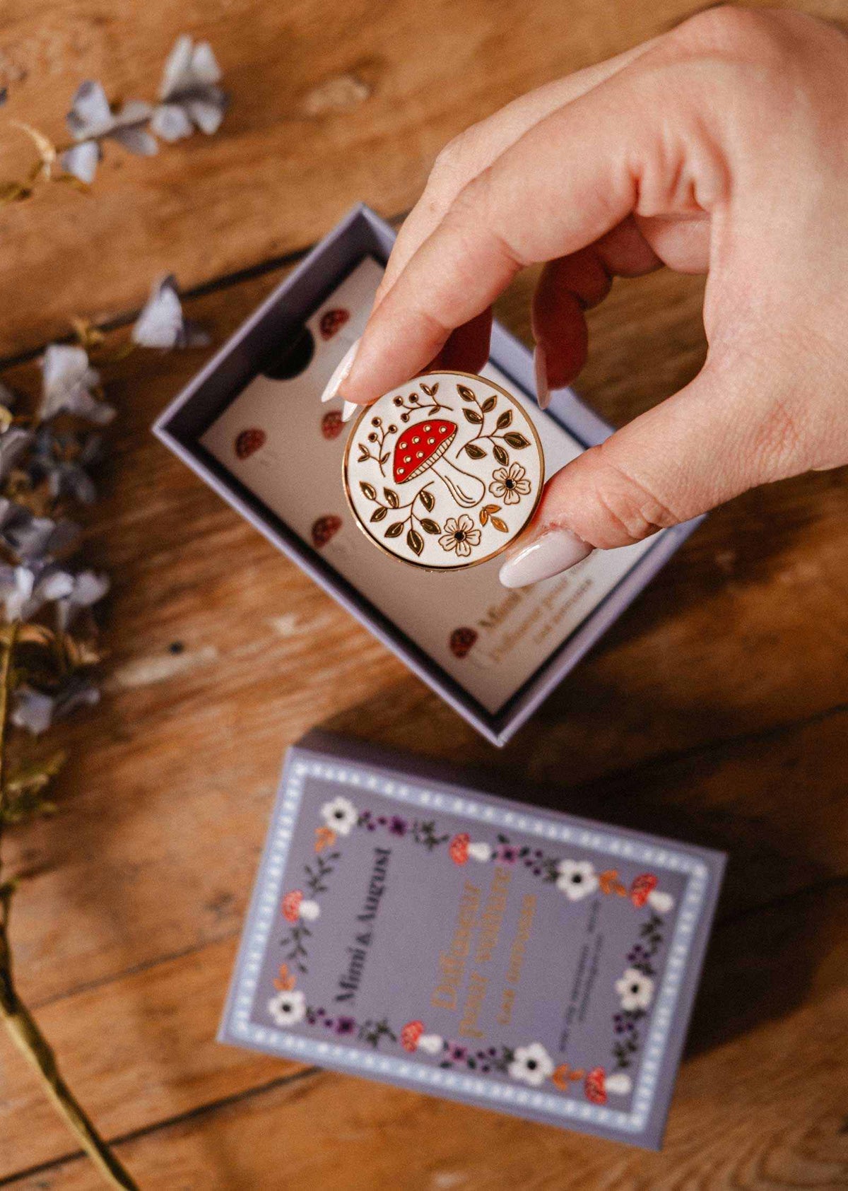 Diffuseur pour voiture Champignon rond en émail crème, illustré de champignons rouges, de fleurs et de feuillages, avec finition dorée.