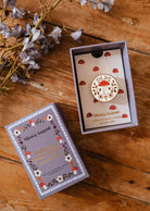 Diffuseur pour voiture Champignon en émail crème et doré, décoré d’un champignon rouge et de fleurs, dans son coffret illustré.