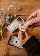 Diffuseur pour voiture Champignon en métal émaillé crème et doré, orné d’un champignon rouge et de motifs floraux.