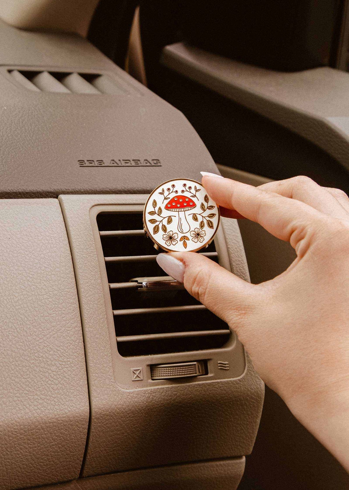Diffuseur pour voiture Champignon rond en émail crème, décoré d’un champignon rouge, de fleurs et de feuillages dorés.