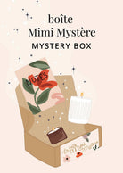 Une boîte ouverte illustrée étiquetée « Boîte Mystère Mimi » de Mimi & August contient un carnet avec une fleur rouge, une petite bougie et une bougie blanche cannelée. Le texte au-dessus indique « Mimi Mystery Box », mettant en valeur ce coffret cadeau trié sur le volet.