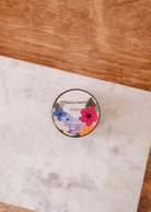 A round tin labeled "Mimi & August" with a colorful floral design sits on a marble surface, showcasing the Palace – 2 oz luxury soy candle, hand-poured in Montreal.