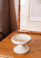 Bougeoir en céramique blanc cassé, à la forme de coupe sur pied et au fini moucheté artisanal.