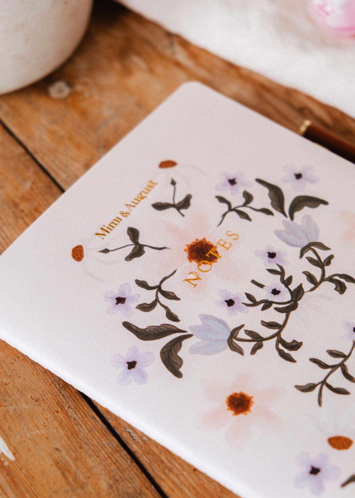 The Rosie Notebook by Mimi & August, made from recycled paper and featuring a charming floral design, rests on a wooden surface.