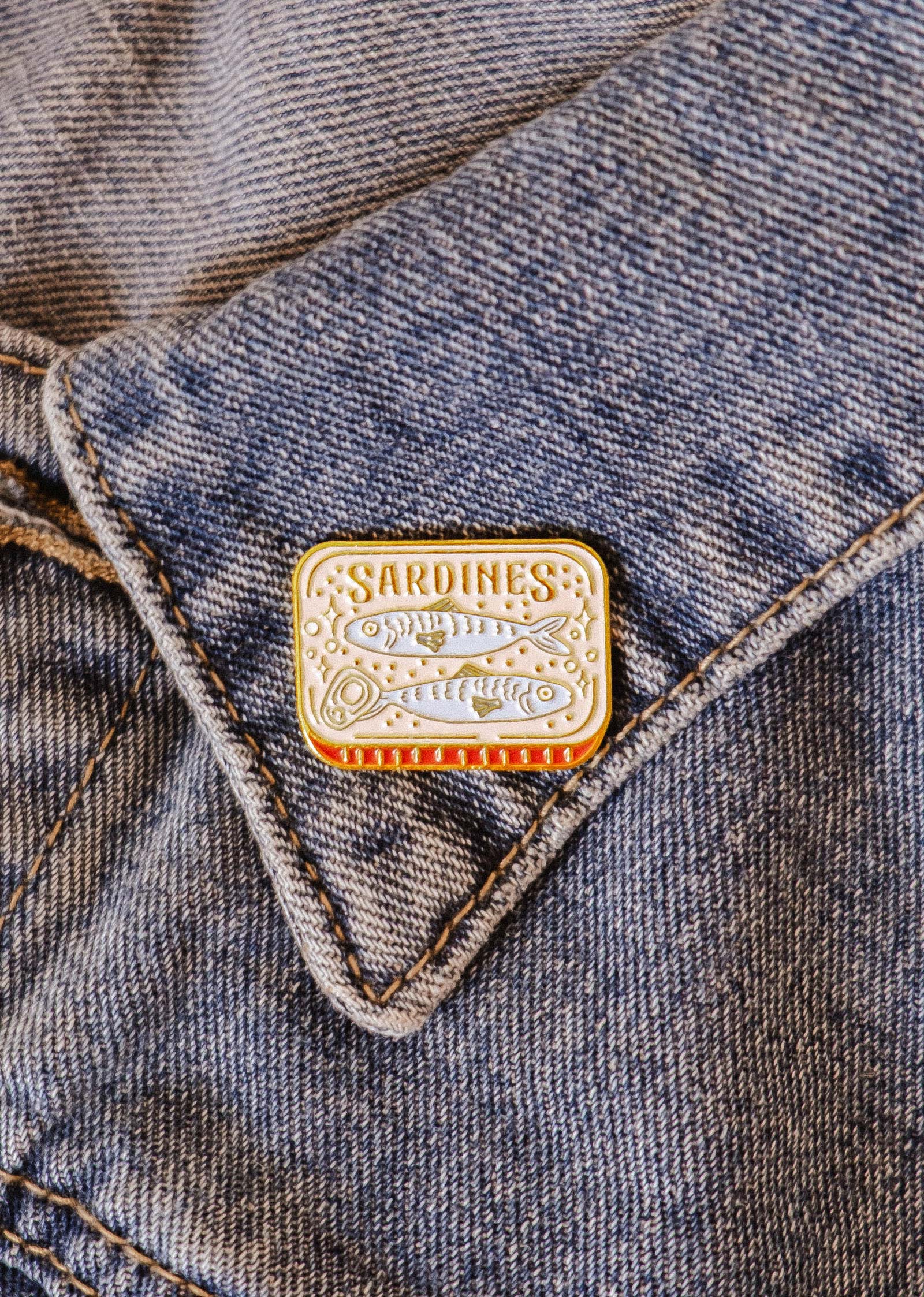 The Cozy Sardines Enamel Pin by Mimi & August, designed in Montreal, adds a touch of personality and charm to your jean pocket.