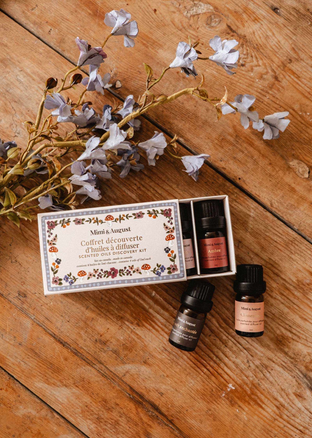 Coffret d’Huiles Parfumées, quatre flacons ambrés avec étiquettes et boîte illustrée à motifs floraux.