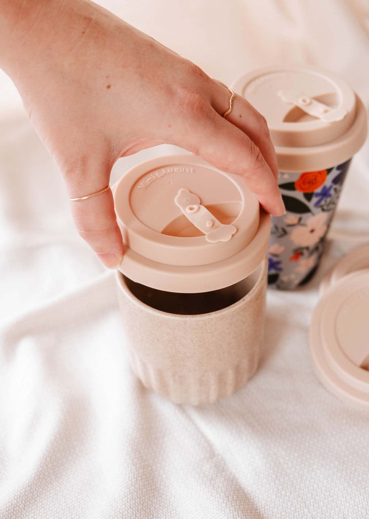 A person holding a Cafe Yo cup with a recyclable Mimi Silicone Lid by Mimi & August on it.