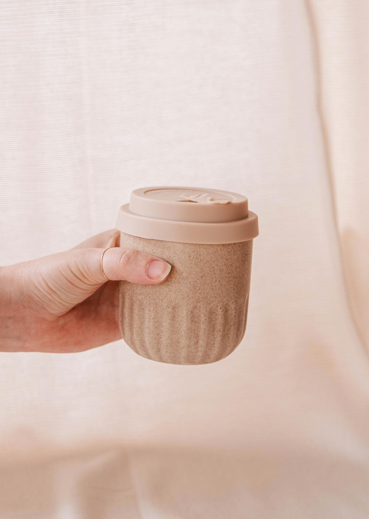 A person holding a Mimi & August Cafe Yo cup with a Mimi Silicone Lid.