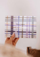 Une main tient une boîte « Crée ton kit découverte » de Mimi & August au motif tartan pastel, contenant des lampions de cire de soja naturelle.