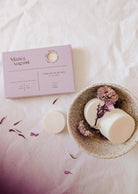 A speckled bowl with two Mimi & August Soy Wax Melts - Lilac and dried flowers sits beside a lavender box on a white surface, providing an eco-friendly, long-lasting fragrance for your space.