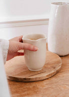 Bougie Orange Épicée dans une tasse en céramique crème mouchetée, au rebord ondulé en forme de pétales, sans anse.