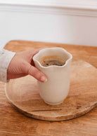 Bougie Orange Épicée dans une tasse en céramique crème mouchetée, au rebord ondulé en forme de pétales.