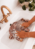 a person washing a mimi and august swimsuit in a sink.