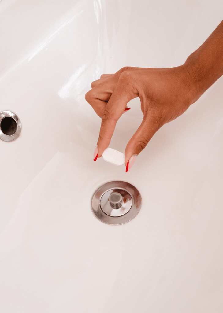 a hand is holding a tablet of soap in front of a sink by mimi and august