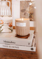 A Tulipa - Reusable Candle by Mimi & August on a small wooden stand, placed atop a stack of books with titles "minimalista" and "this is home" on a cozy tabletop.