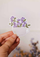 Vinyl sticker of a warm white teacup with purple blooms, durable and water-resistant
