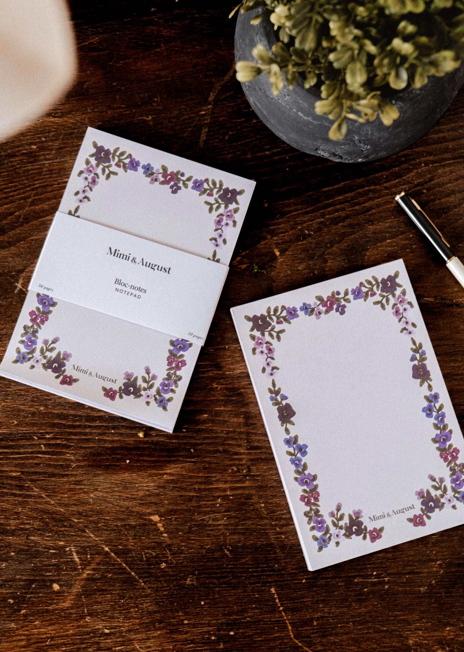 Two Wildflowers floral notepads by Mimi & August on a wooden table with a pen and potted plant, illustrated covers on display.