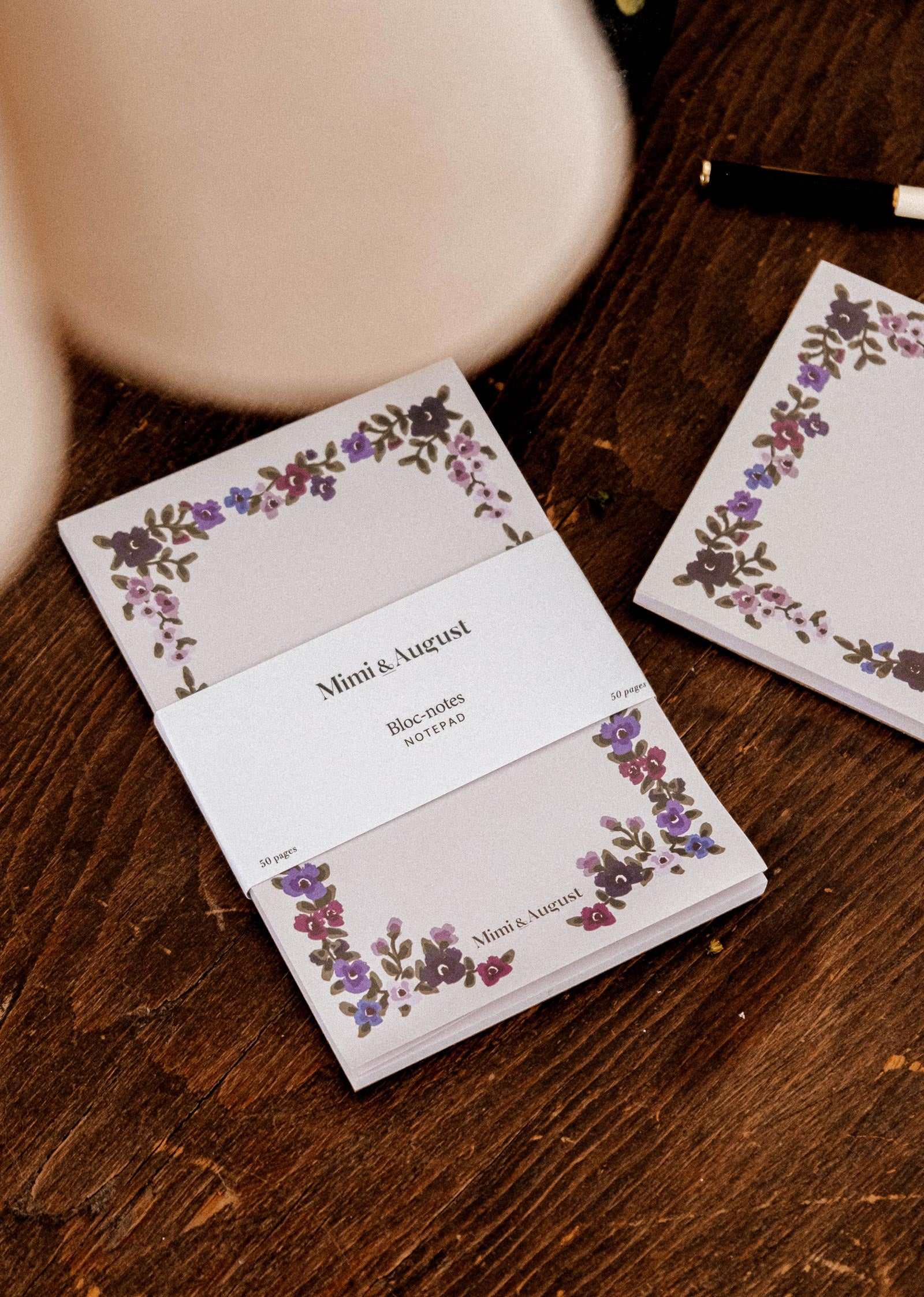 Wildflowers floral notepad by Mimi & August on a wooden surface beside a matching illustrated note card and a pen.
