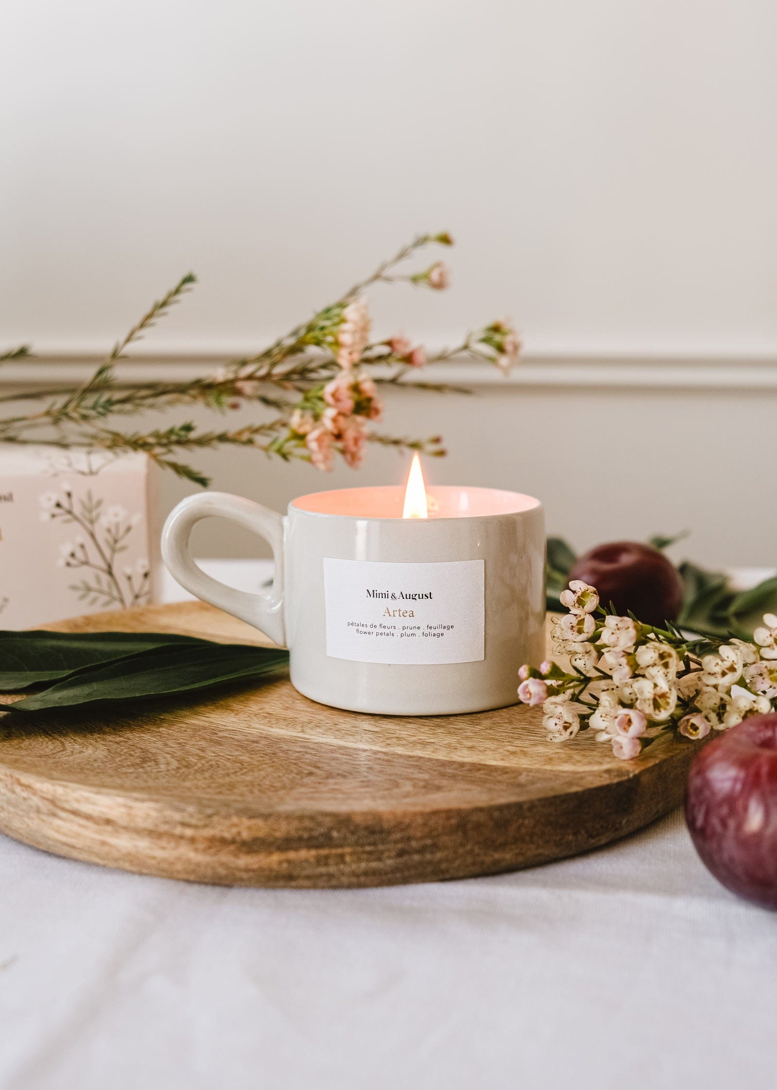 A Mimi & August - Artea Reusable Candle sits on a wooden cutting board next to some flowers.