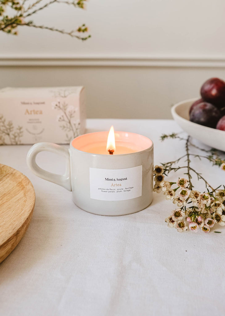 An Mimi & August - Artea Reusable Candle sits next to a bowl of plums, filling the room with its fragrance.