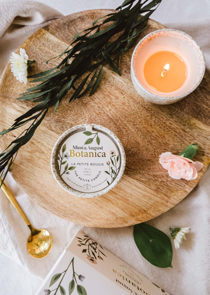 A Mimi & August Botanica - Reusable Candle and a small book placed on a wooden tray decorated with flowers and green leaves, creating a serene ambiance.