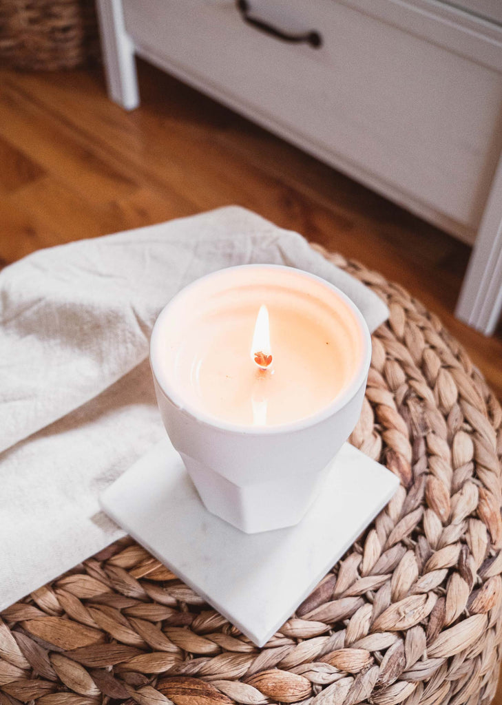 A Brooklyn - Reusable Candle from Mimi & August sits on top of a wicker basket, emitting a fragrant aroma.