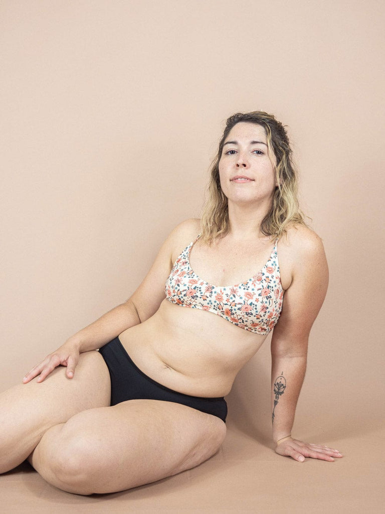 A woman posing in a Chichi Amour Bralette Bikini Top from the Mimi & August collection on a beige background, showcasing an adjustable top and swimwear.