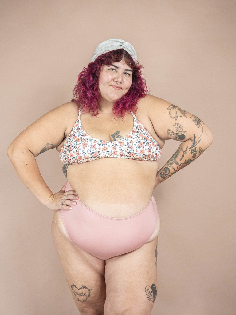Une femme portant un haut de bikini rose Chichi Amour Bralette de la collection de maillots de bain Mimi & August ajuste son haut réglable pour une photo.