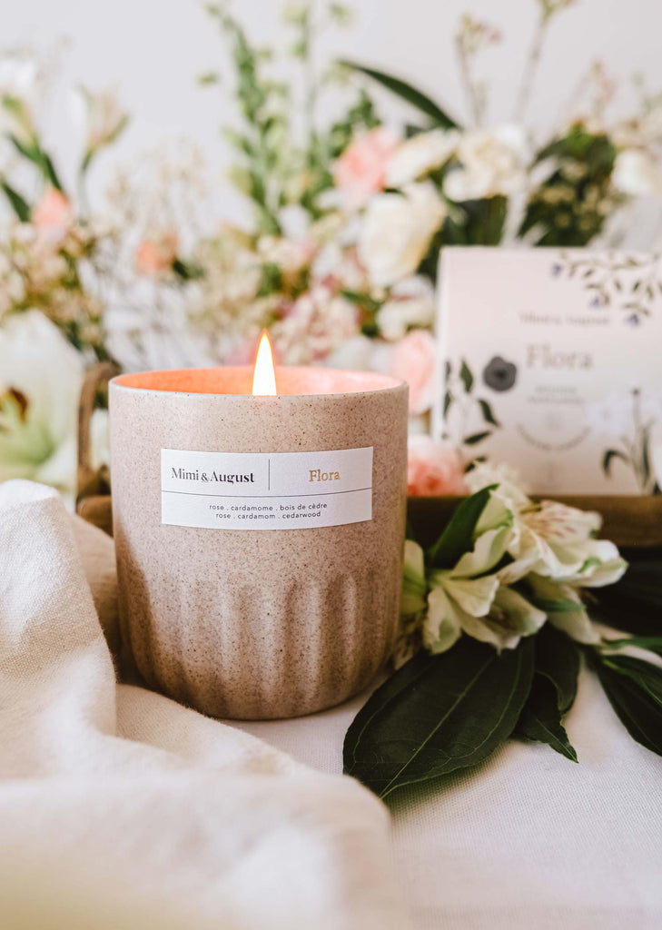 The Flora - Reusable Candle by Mimi & August showcases a floral scent near a bouquet of roses.