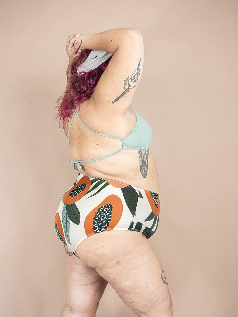 A woman in a Paloma Papaya high waisted bikini bottom by Mimi & August with a tattoo on her back.