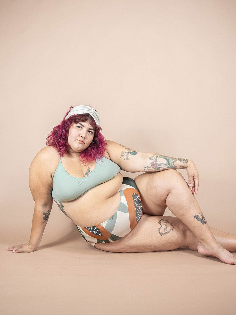 A woman in a Paloma Papaya high waisted bikini bottom by Mimi & August, laying on a beige background.