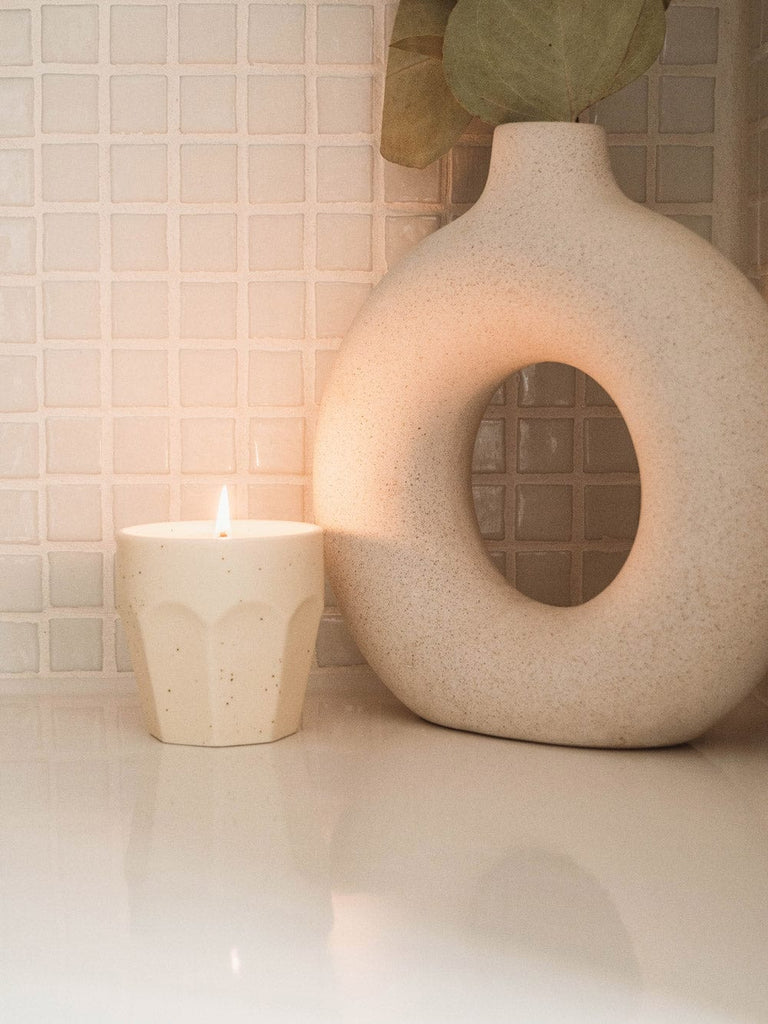 Un vase blanc avec, à côté, une bougie Mare - Reusable Candle de Mimi & August, avec une touche de menthe.