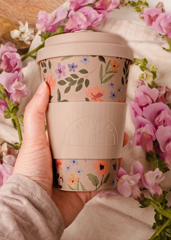 reusable bamboo cup in the hand and with lots of summer flowers around