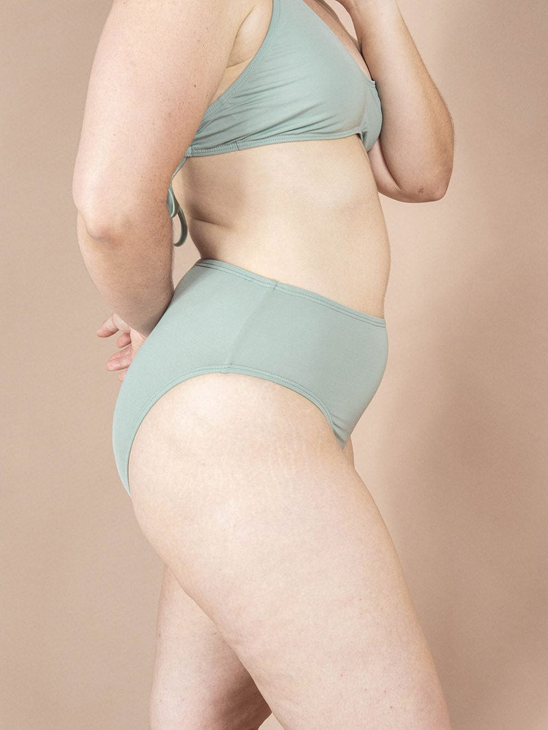 Une femme en bikini vert avec un bas de bikini Tucan Agave à jambe haute et taille haute de la marque Mimi & August pose.