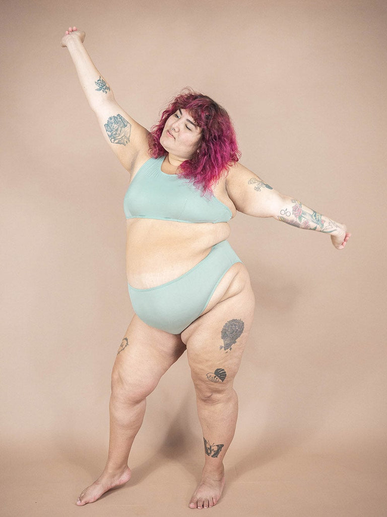 A woman in a Tucan Agave high leg & high waist bikini bottom in the brand Mimi & August with tattoos.