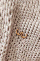Épinglette Seins en laiton doré, au design minimaliste, délicatement posée sur un fond de tissu texturé