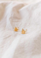 Cafecito gold plated earrings shaped like coffee cups on beige fabric background