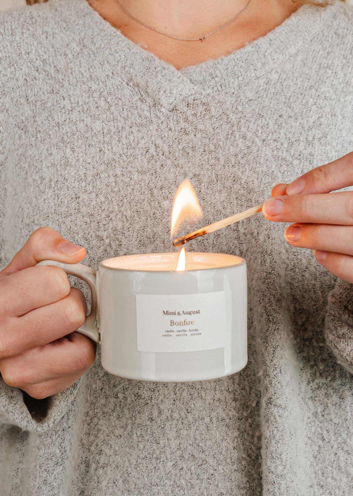 Person lighting a Bonfire campfire candle in a reusable ceramic mug with a matchstick