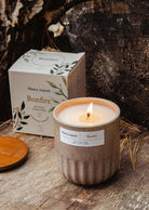 Lit Bonfire reusable soy campfire candle in ceramic cup with packaging on wooden surface outdoors