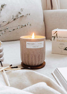 Lit eucalyptus candle in a reusable ceramic cup on a cozy surface with eucalyptus leaves in the background