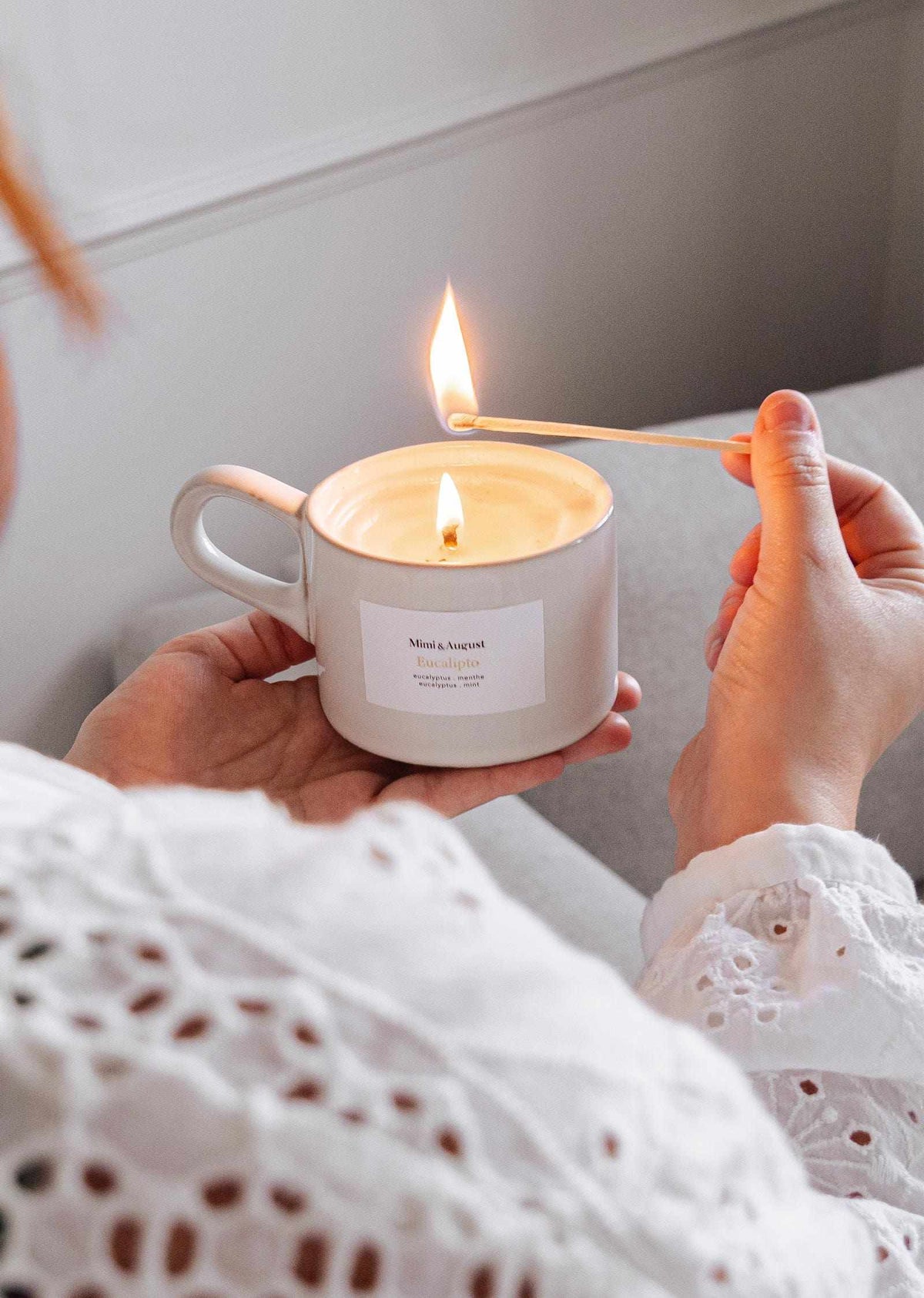 Person lighting a reusable eucalyptus candle in a ceramic cup with a wooden matchstick