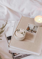 Eucalyptus candle in reusable ceramic cup on stack of books with soft natural lighting