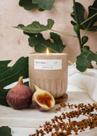Burning fig candle in a textured cup with figs and green leaves background
