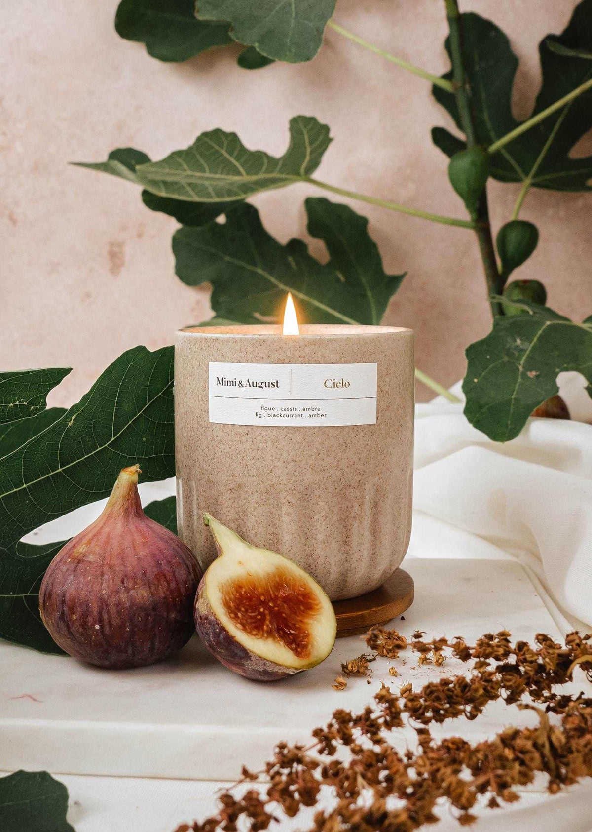 Burning fig candle in a textured cup with figs and green leaves background