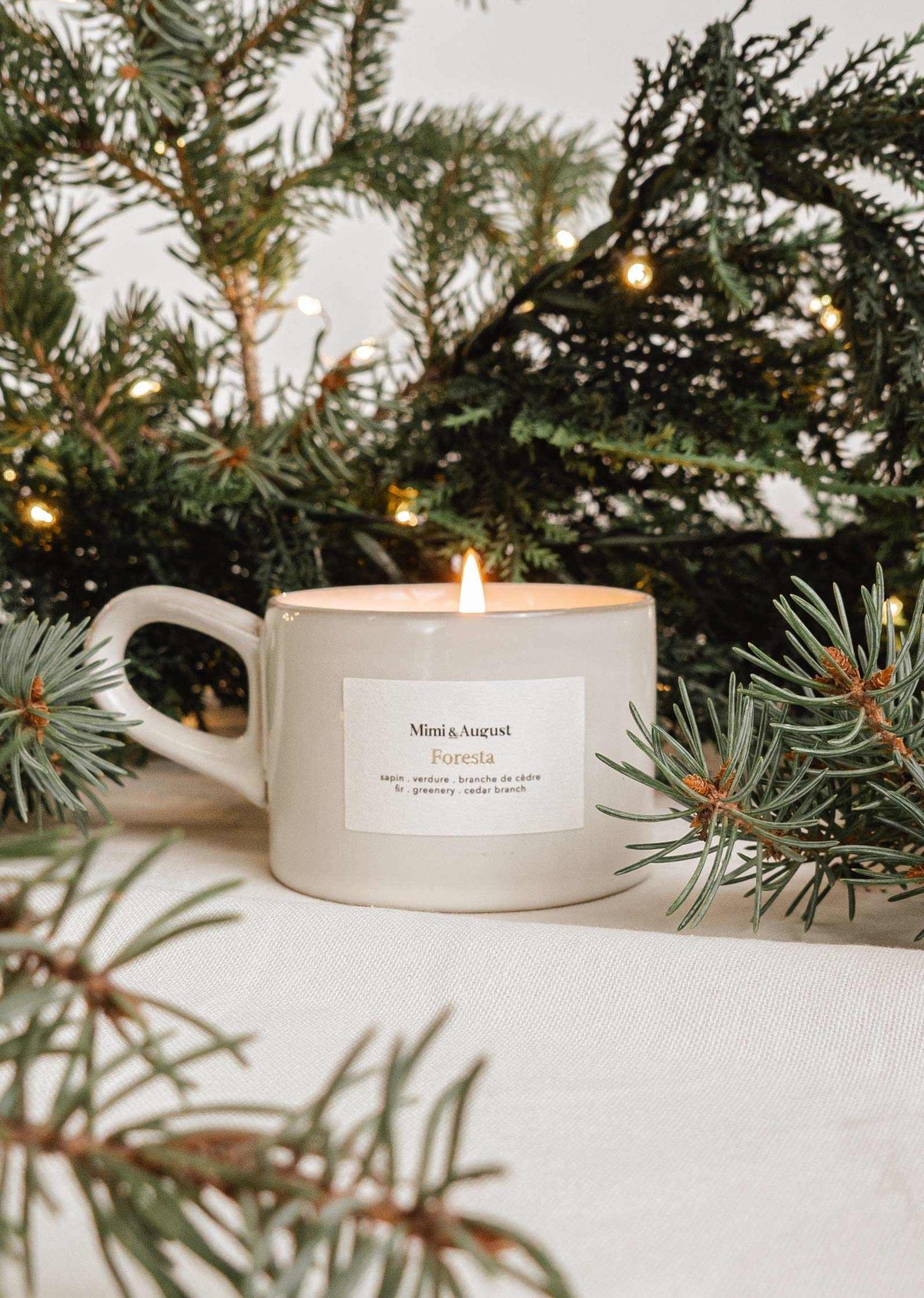 Foresta fir tree candle in a speckled gray handle cup with forest fir branches and warm lights background